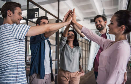 Beautiful young business people in casual clothes are putting hands together and smiling while standing corridor in business centerの写真素材