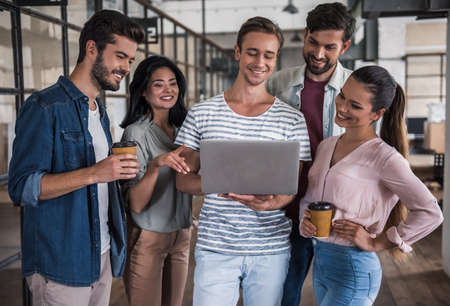 Beautiful young business people in casual clothes are using a laptop and smiling while standing corridor in business centerの写真素材