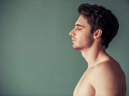 Side view of handsome young man with bare torso standing with closed eyes on gray backgroundの写真素材