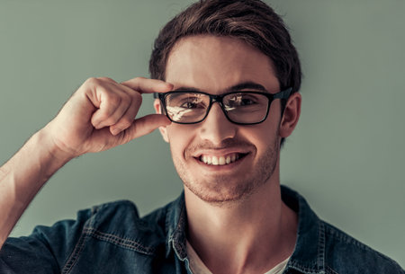 Handsome young man in casual clothes and eyeglasses is looking at camera and smiling, on gray backgroundの写真素材