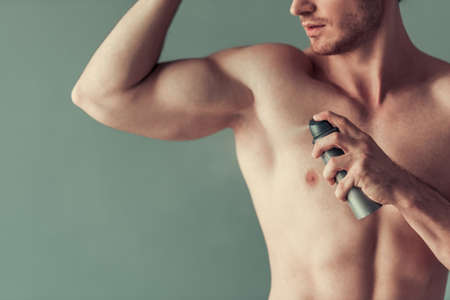 Cropped image of handsome young man with bare torso using a spray deodorant, on gray backgroundの写真素材