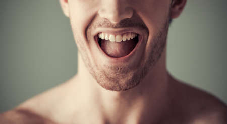 Cropped image of handsome young man screaming, on gray backgroundの写真素材