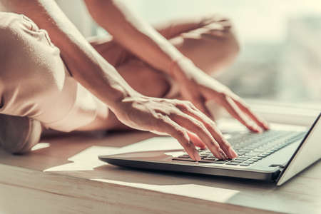 Cropped image of beautiful Afro American girl using a laptop while sitting on window sill at homeの写真素材
