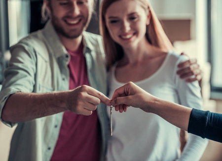 Beautiful young couple is taking a key, hugging and smiling while moving into new apartment