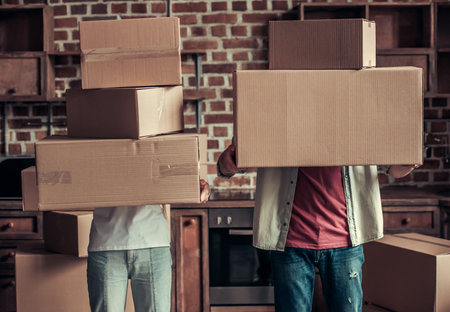 Beautiful young couple is holding cardboard boxes while moving into new apartment
