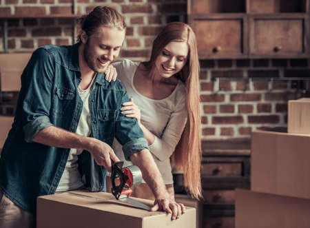 Beautiful young couple is packing cardboard boxes and smiling while moving into new apartmentの写真素材