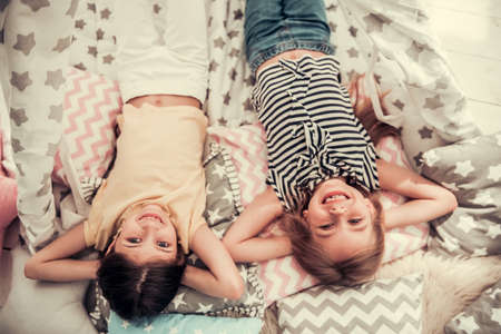 Top view of two cute little girls looking at camera and smiling while playing together at homeの写真素材