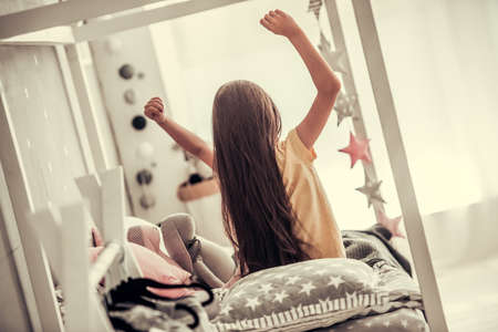 Back view of little girl stretching and yawning while waking up in her room at homeの写真素材