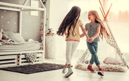 Two happy little girls are dancing and smiling while playing in children's room at homeの写真素材