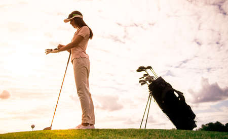 Full length portrait of beautiful young woman holding a golf club while standing on golf courseの写真素材