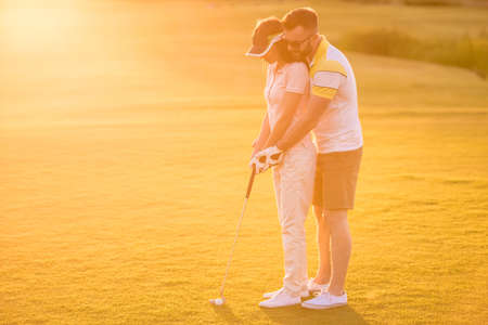 Beautiful young couple is hugging and smiling while playing golfの写真素材