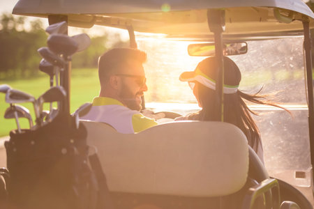 Back view of beautiful couple talking and smiling while driving a golf cartの写真素材