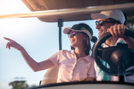 Beautiful couple is talking and smiling while driving a golf cartの写真素材