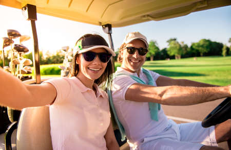 Beautiful couple is looking at camera and smiling while driving a golf cartの写真素材