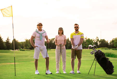 Two men and a woman are holding golf clubs and looking at camera while standing on golf courseの写真素材