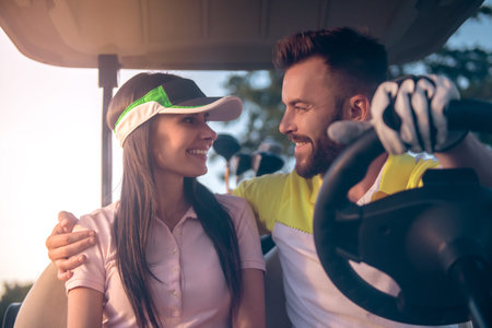 Beautiful young couple is talking and smiling while driving a golf cartの写真素材
