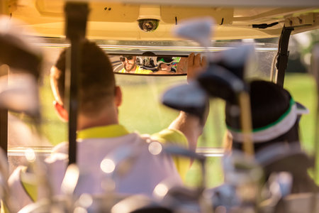 Back view of beautiful couple driving a golf cart, golf clubs in the foregroundの写真素材