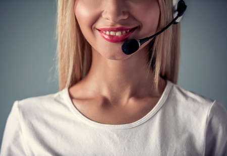 Cropped image of beautiful young woman in headset smiling, on gray backgroundの写真素材