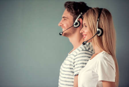 Side view of beautiful young couple in headsets looking forward and smiling, on gray backgroundの写真素材