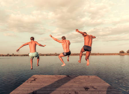 Handsome guys are jumping from pier into the lake, beautiful viewの写真素材
