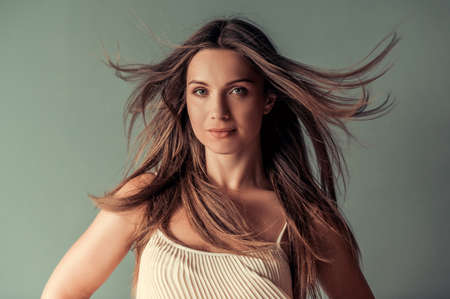 Beautiful woman with streaming hair is looking at camera and smiling, on gray backgroundの写真素材