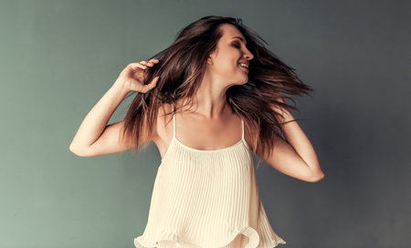 Beautiful woman is playing with her hair and smiling, on gray backgroundの写真素材