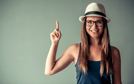 Beautiful woman in casual clothes and stylish hat is pointing upward, posing at camera and smiling,...