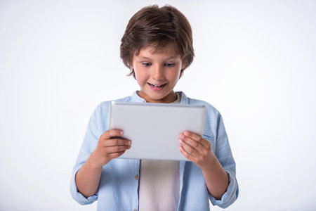 Attractive little boy is using a digital tablet and smiling, on light backgroundの写真素材