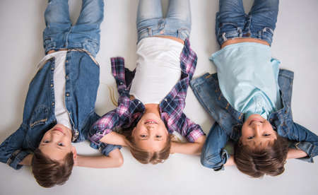 Top view of cute kids looking at camera and smiling while lying on the floor with hands behind headsの写真素材
