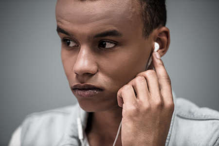 Stylish Afro American guy in earphones is listening to music, on gray backgroundの写真素材
