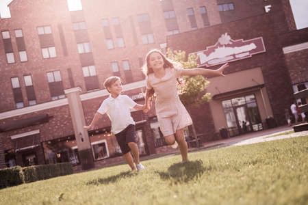 Cheerful kids are holding hands, running and smiling while playing together outdoorsの写真素材