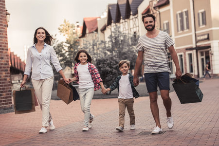 Beautiful parents and their cute little kids are carrying shopping bags, holding hands and smiling...