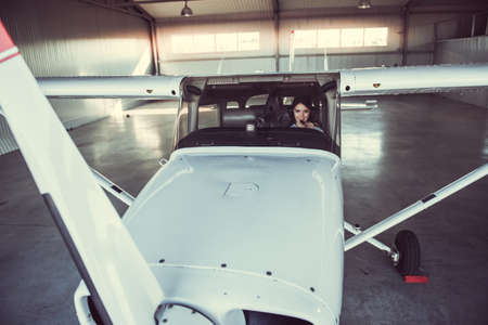 Beautiful woman-pilot in aviation headset is looking at camera and smiling while sitting in aircraftの写真素材