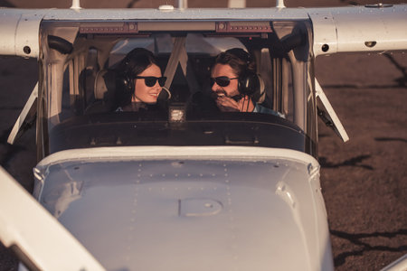 Beautiful couple in aviation headsets is looking at each other and smiling while sitting in aircraft...