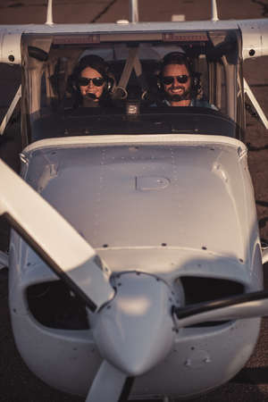 Beautiful couple in aviation headsets is looking at camera and smiling while sitting in aircraft ready to flyの写真素材