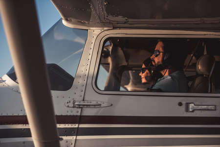 Beautiful couple in aviation headsets is sitting in aircraft ready to flyの写真素材