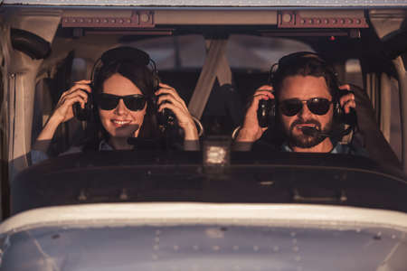 Beautiful couple in aviation headsets is looking at camera and smiling while sitting in aircraft ready to flyの写真素材