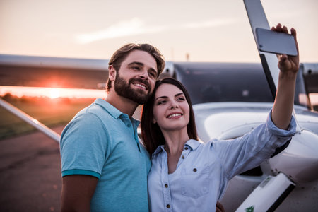Beautiful romantic couple is using a smart phone and smiling while doing selfie on take-off ground...