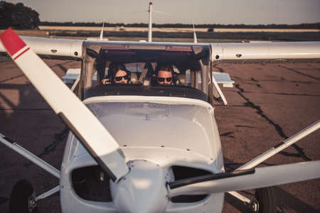 Beautiful couple in aviation headsets is sitting in aircraft ready to flyの写真素材