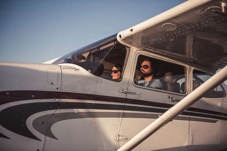 Beautiful couple in aviation headsets is sitting in aircraft ready to flyの写真素材