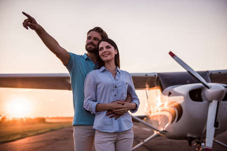Beautiful romantic couple is hugging and smiling while enjoying the view on take-off ground near the aircraftの写真素材