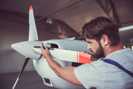 Handsome bearded mechanic in uniform is examining an aircraft in hangarの写真素材