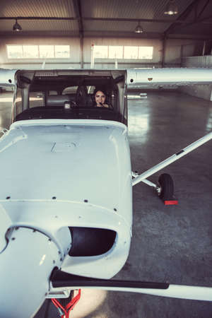 Beautiful woman-pilot in aviation headset is looking at camera and smiling while sitting in aircraftの写真素材
