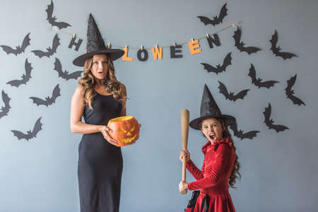 Cute little girl and her mom dressed for Halloween party and with accessories are posing at cameraの写真素材