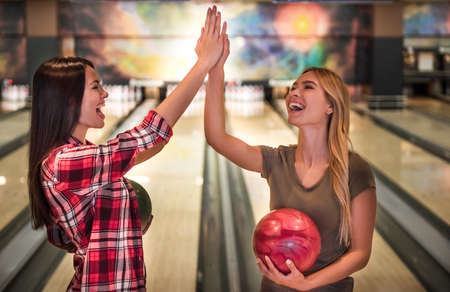 Beautiful girls are holding bowling balls, giving high five and smiling ready to playの写真素材