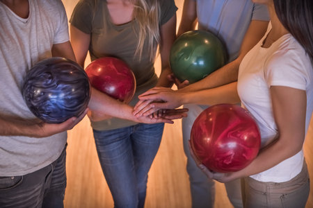 Cropped image of young friends holding balls and putting hands together while playing bowlingの写真素材
