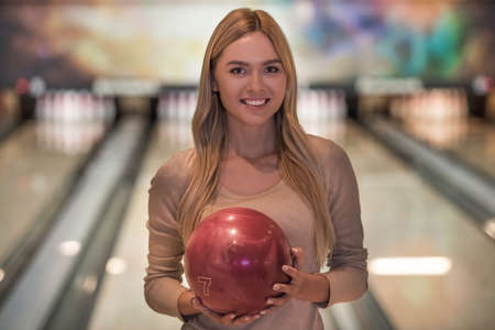 Attractive blonde girl is holding a bowling ball, looking at camera and smiling ready to play bowlingの写真素材