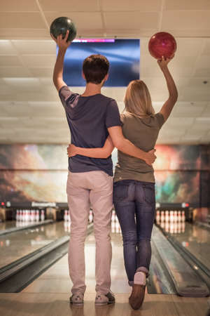 Back view of beautiful girl and handsome guy holding bowling balls and hugging while playingの写真素材