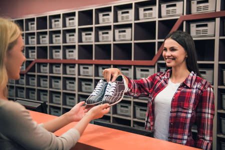 Beautiful girl is offering a pair of bowling shoes to the client and smilingの写真素材