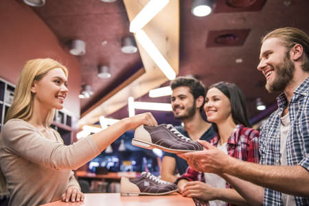 Cheerful young people are taking bowling shoes and smiling ready to play bowlingの写真素材